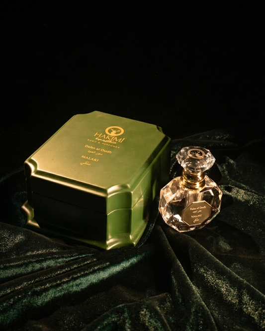 Green perfume box and clear perfume bottle on a dark green fabric background