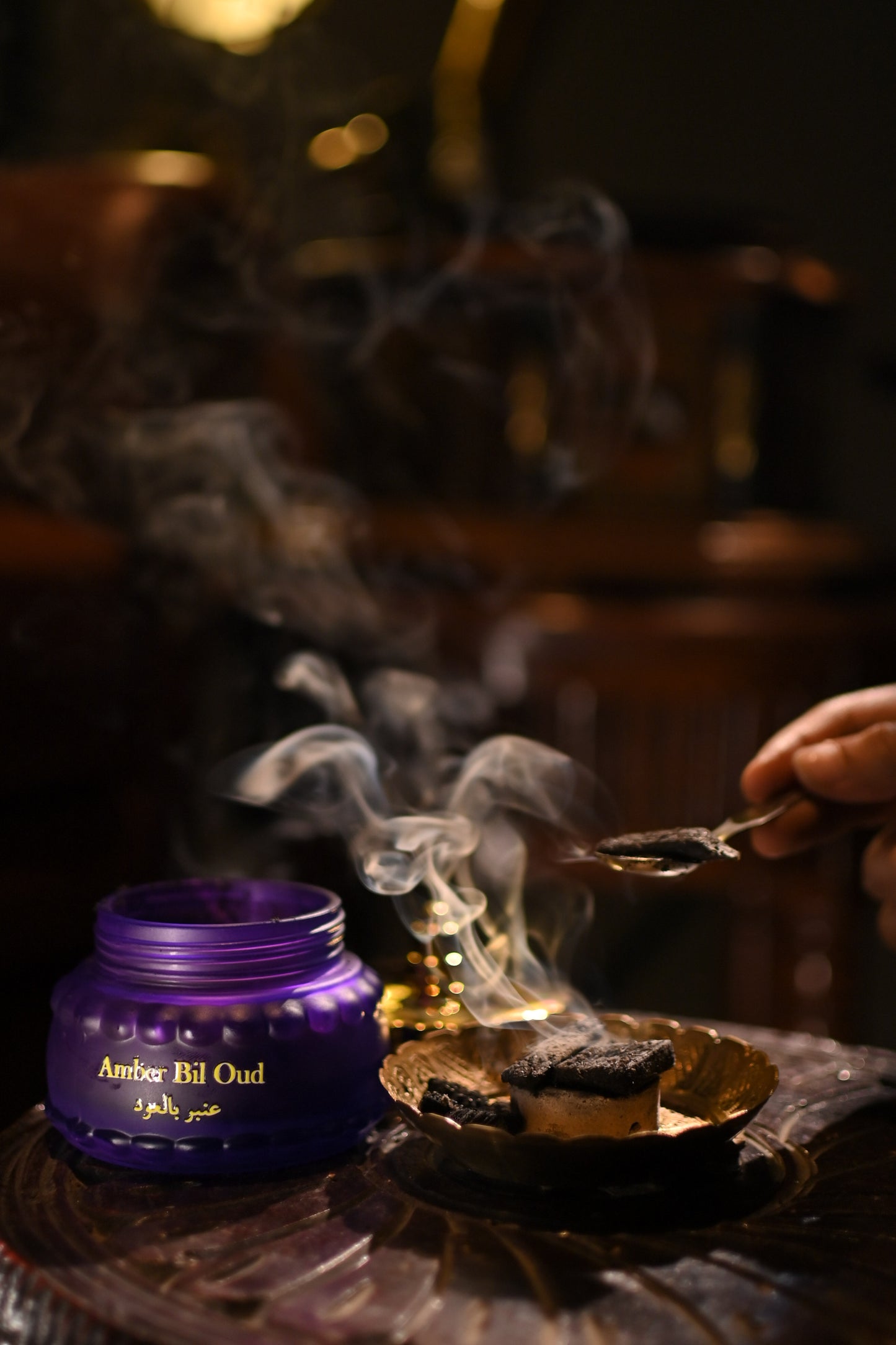 Purple container labeled 'Amber Fil Oud' with smoke on a dark background