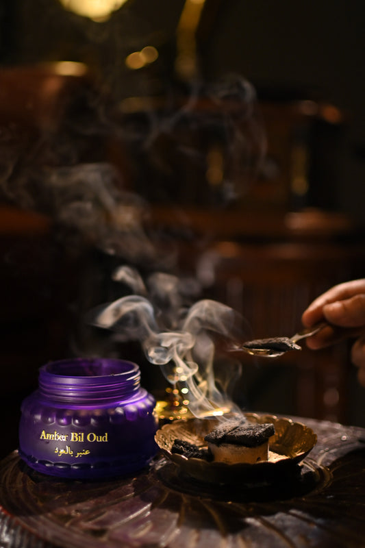 Purple container labeled 'Amber Fil Oud' with smoke on a dark background