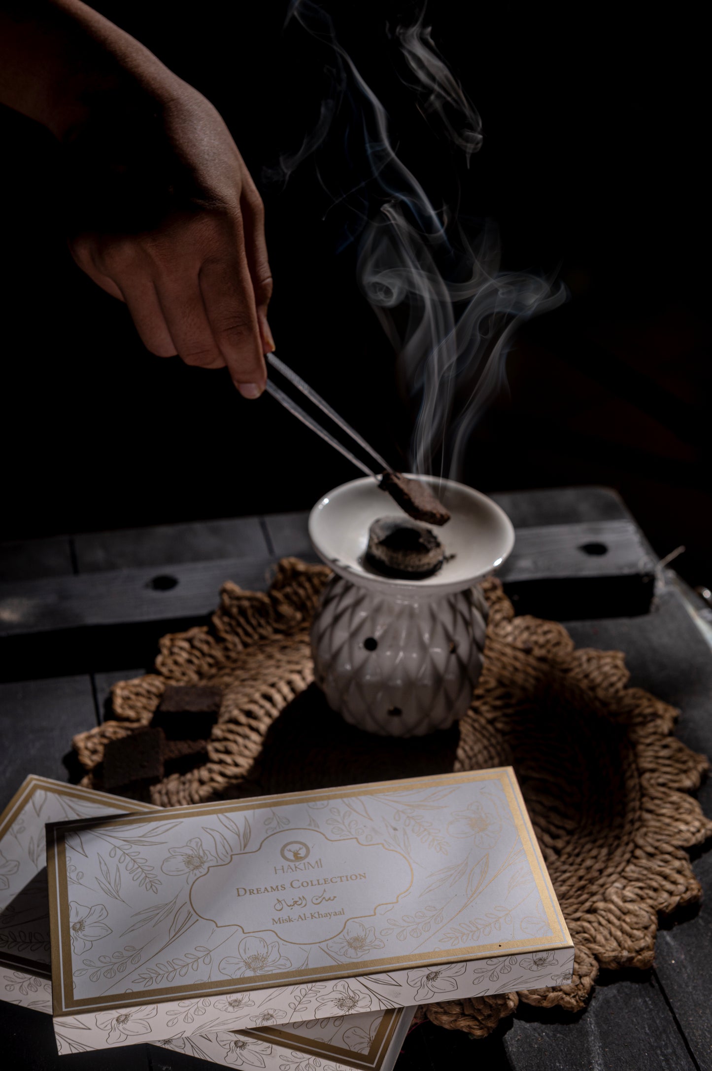Incense stick being lit with smoke rising from a small incense burner on a textured surface.