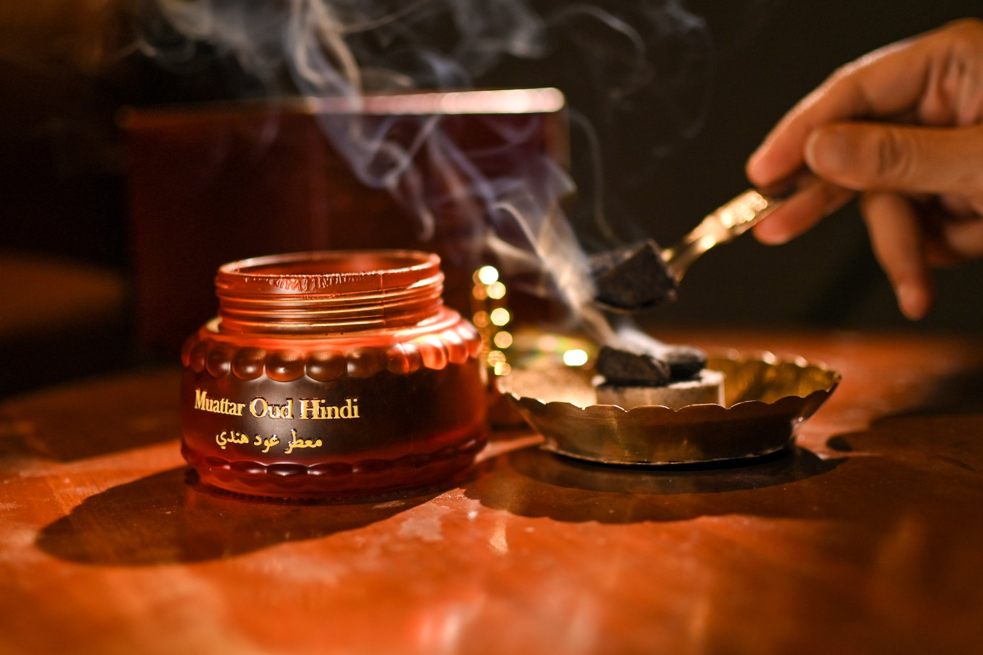 Matter Oud Hindi incense being burned with smoke rising from a container on a wooden surface.
