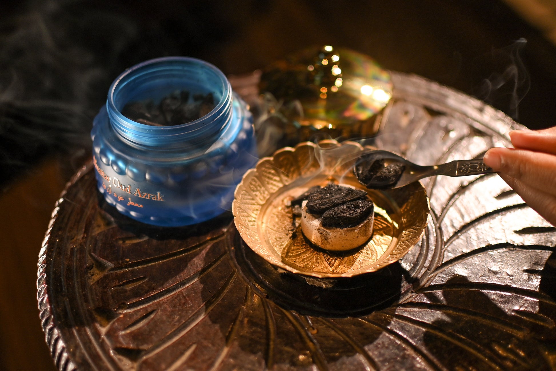 Blue container labeled 'Narghile Charcoal' on a decorative metal tray with smoking materials.
