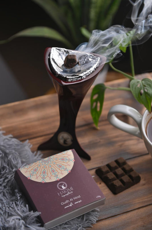 Incense burner with smoke, a purple box labeled 'Jewelled' on a wooden surface with plants in the background.