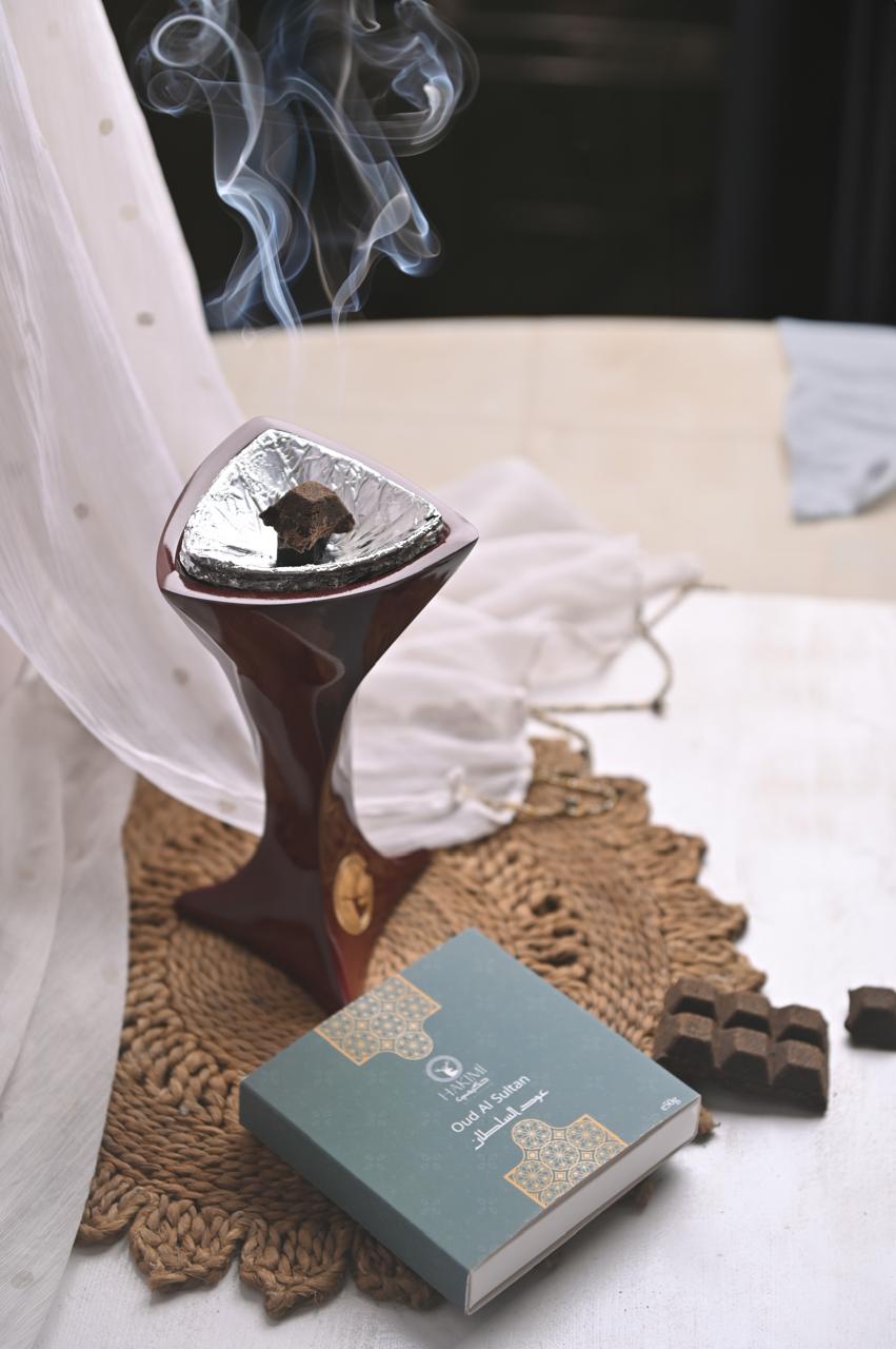 Incense burner with smoke, a book, and chocolates on a textured surface.