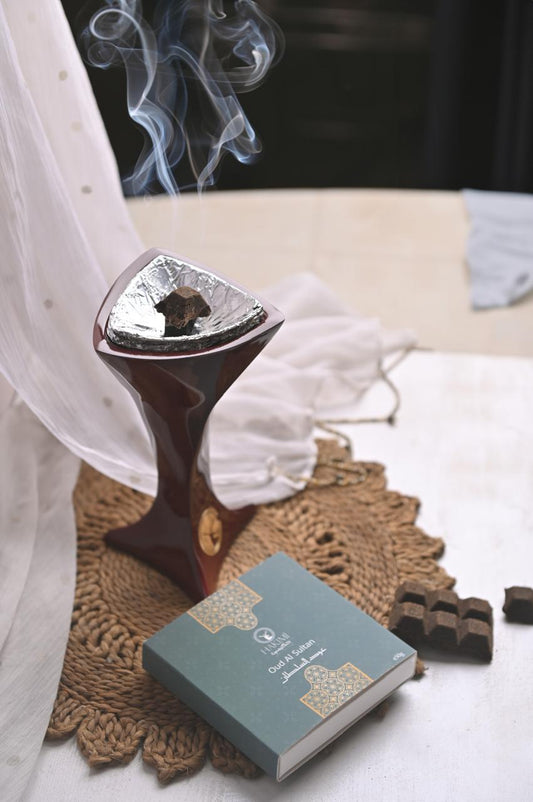 Incense burner with smoke, a book, and chocolates on a textured surface.