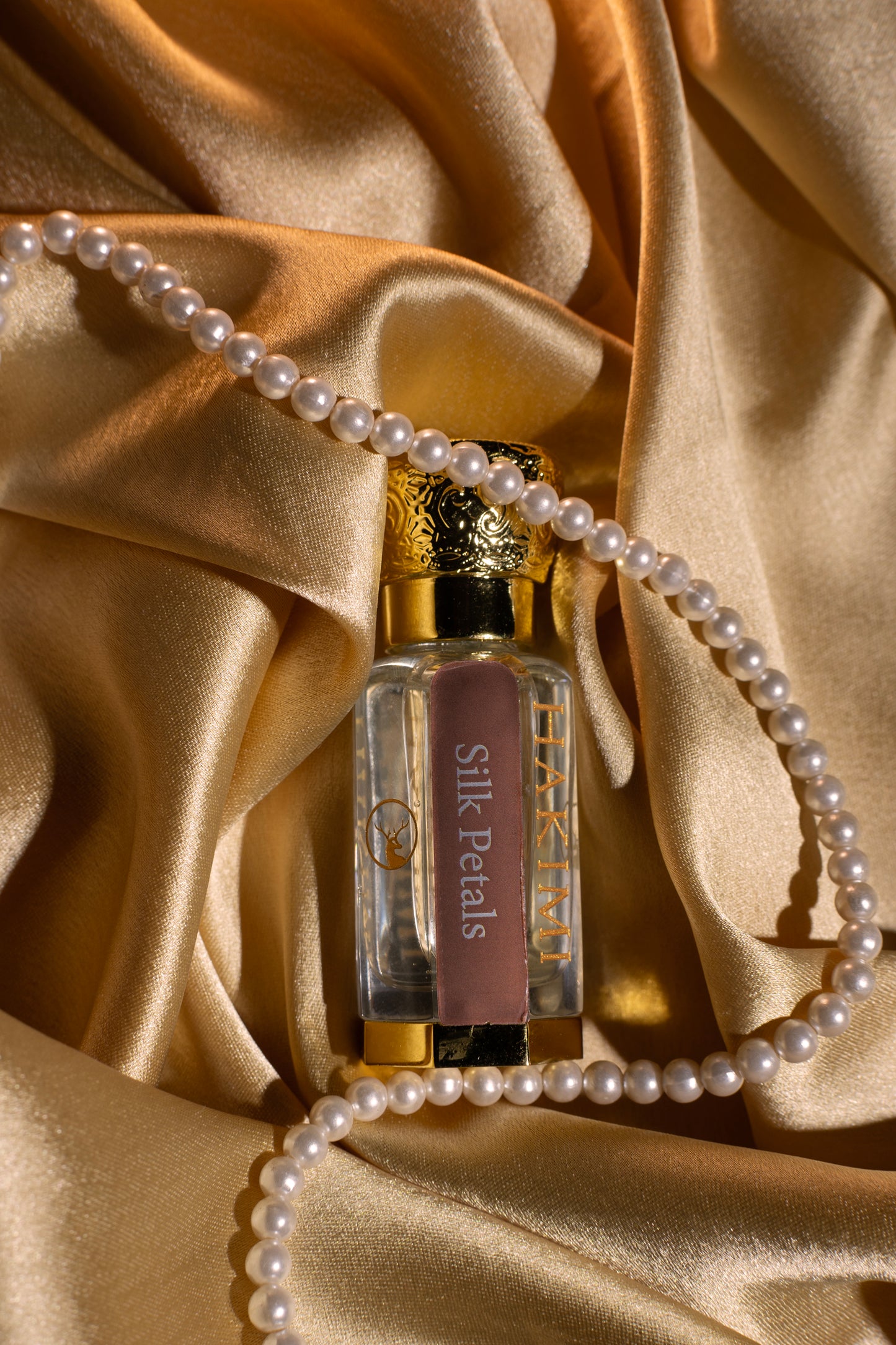 Perfume bottle with 'Silk Petals' branding on a gold satin background with pearls.
