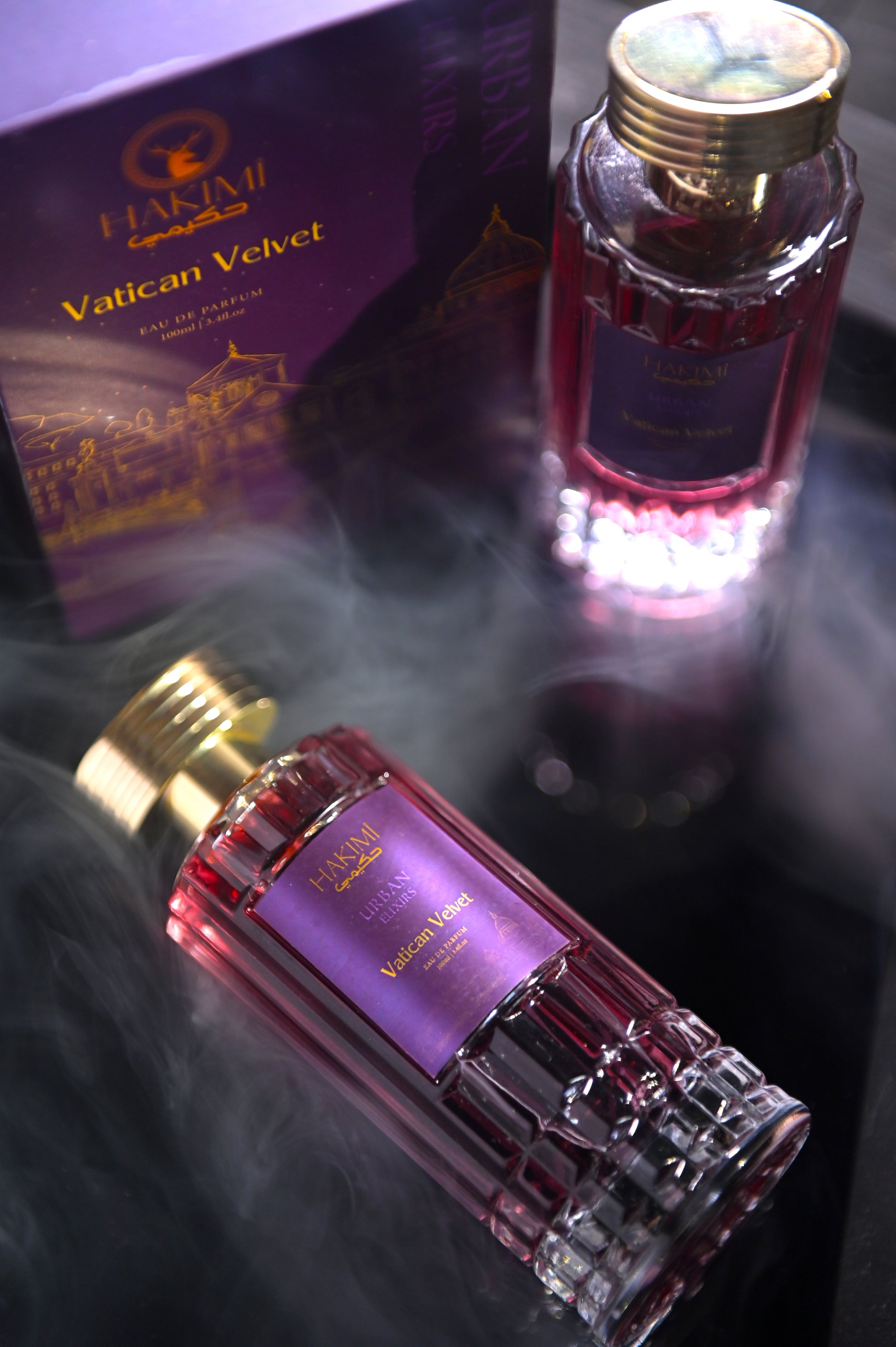 Two bottles of Vatican Velvet perfume with a box in the background on a reflective surface.