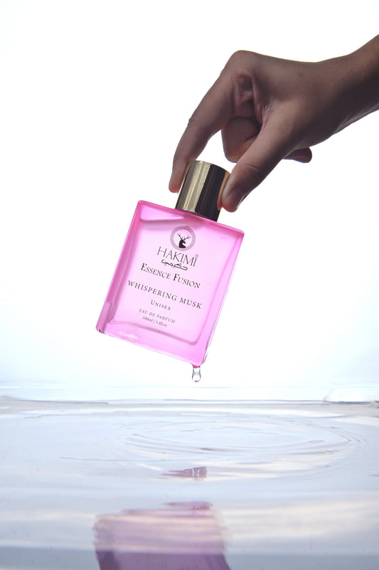 Pink perfume bottle with gold cap held by a hand above water